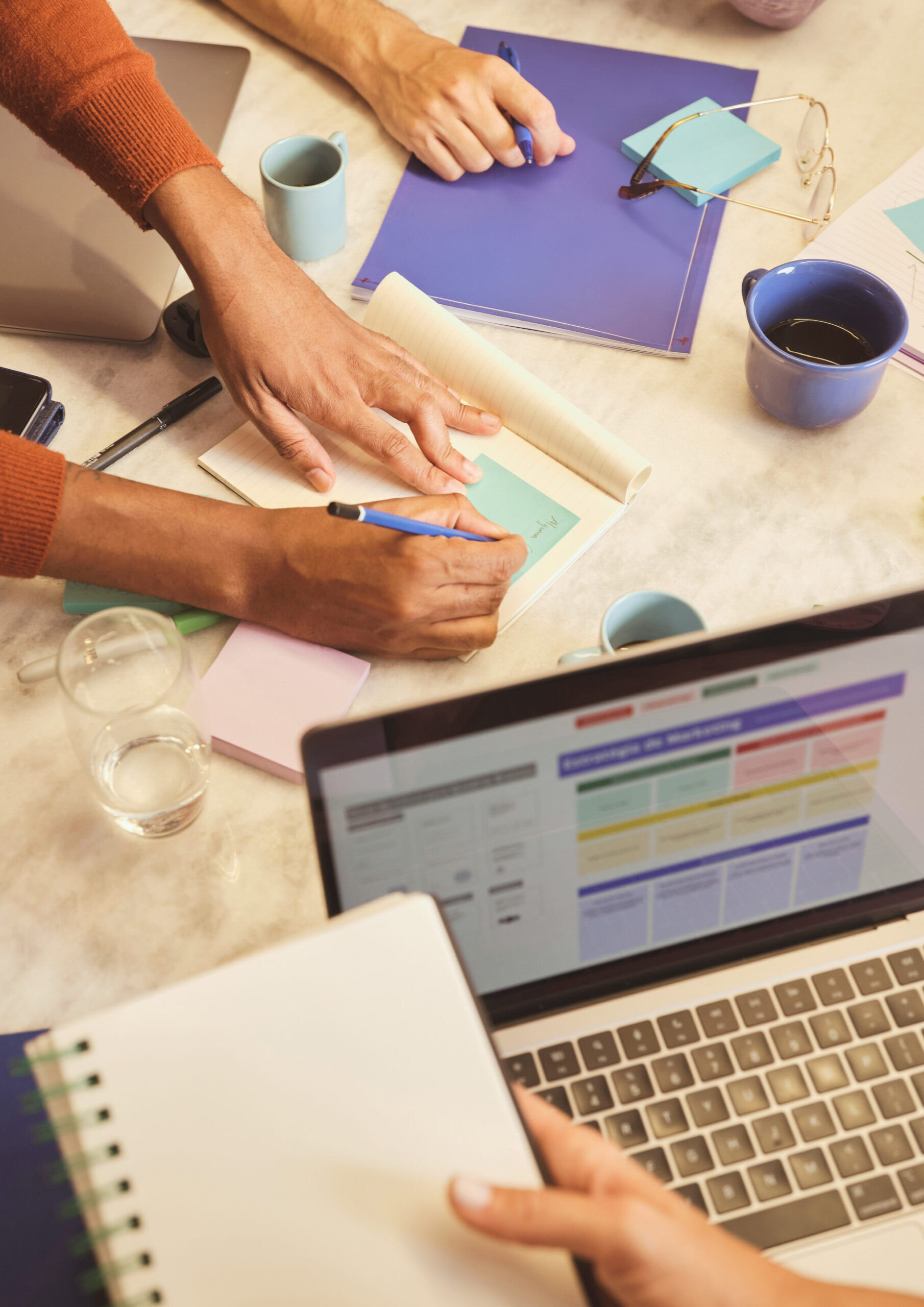Two people collaborating over a laptop with notes and coffee at a desk.