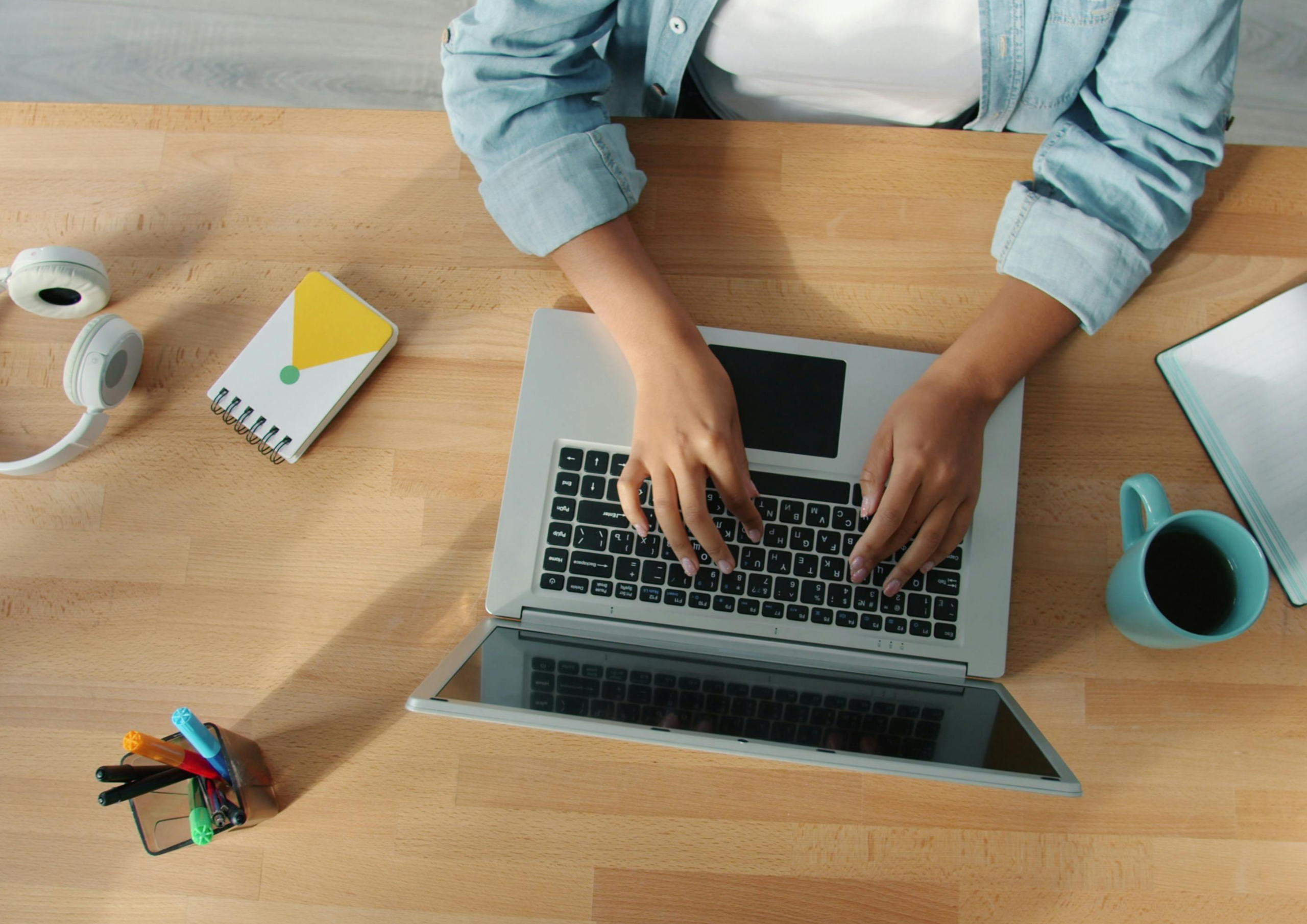 Person typing on a laptop at a desk with coffee, notebook, and headphones